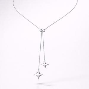 Könnte beinhalten: Eine silberfarbene Halskette mit einer filigranen Kette und zwei herabhängenden vierzackigen Sternanhängern. Die Halskette hat ein schlichtes Design mit einer verschiebbaren Perlenverstellung. Der Schmuck ist vor einem weißen Hintergrund platziert.