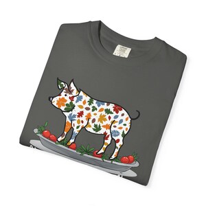 May include: Dark grey t-shirt with a pig illustration. The pig is decorated with colourful autumn leaves and stands on a platter with tomatoes and greenery. The shirt has a Comfort Colors tag.