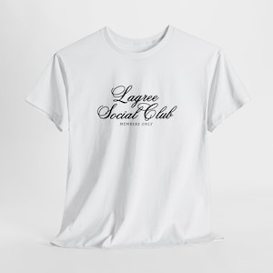 May include: A white t-shirt with the words "Lagree Social Club" in a black, elegant script across the chest. Below the script is the text "MEMBERS ONLY" in a smaller font. The shirt has short sleeves and a crew neck.
