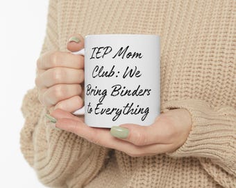 Può includere: Una tazza di ceramica bianca con la scritta "IEP Mom Club: We Bring Binders to Everything" in corsivo nero. La tazza è tenuta da una persona che indossa un maglione beige.