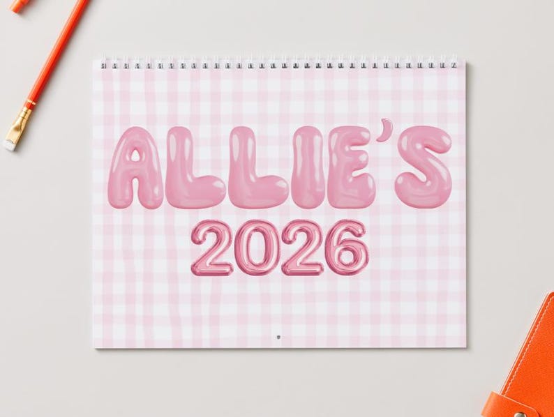 May include: A spiral-bound calendar with a pink gingham pattern background. The text "ALLIE'S 2026" is displayed in a bubble-style font. A red pencil and an orange accessory are visible in the background.