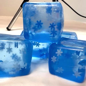 Könnte beinhalten: Vier blaue, durchsichtige Seifenstücke mit Schneeflocken-Designs. Die Seifenstücke sind übereinander gestapelt.