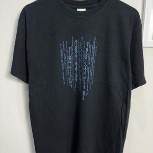 Könnte beinhalten: Schwarzes T-Shirt mit einem blauen und weißen Grafikdruck einer Reihe von 0en und 1en.