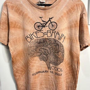 May include: A tie-dye orange t-shirt with a black graphic of a mountain bike and a brain with the text "Bikes on the Brain" and "Cool February 16, 2003".