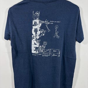 May include: A navy blue short-sleeve t-shirt featuring a white graphic print on the back. The design displays the word DUKE vertically with cartoon figures and text including "GO TO HELL CAROLINA", "OH BRAVE NEW WORLD", and various career labels.