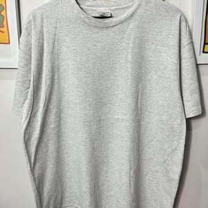 Könnte beinhalten: Ein hellgraues T-Shirt mit Rundhalsausschnitt.