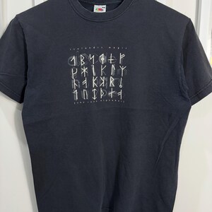 May include: Black t-shirt featuring a white graphic of the Icelandic alphabet, "The Rune Alphabet", in a stylised font.