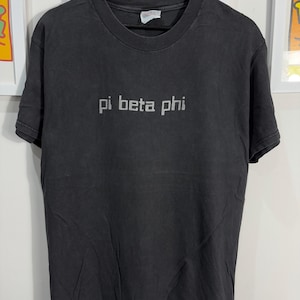 Könnte beinhalten: Ein schwarzes T-Shirt mit dem Aufdruck "pi beta phi" in Weiß auf der Vorderseite.