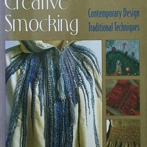 May include: A book titled Creative Smocking: Contemporary Design Traditional Techniques. The cover features a cream-colored garment with blue textured fringe, a landscape illustration, a red fabric square, and a close-up of gold smocking detail.