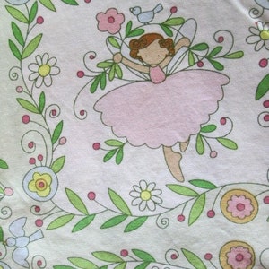 May include: A pink and white fabric with a floral pattern and a fairy illustration. The fairy is wearing a pink dress and has brown hair. The fabric has a white background with green vines and pink flowers.