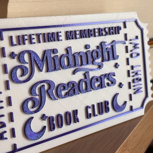 May include: A white and purple 3D-printed sign with the text "LIFETIME MEMBERSHIP Midnight Readers BOOK CLUB Night Owl". The sign is shaped like a ticket with a decorative border, possibly for a book club.