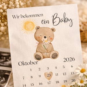 Könnte beinhalten: Baby-Ankündigungskarte mit dem Text "Wir bekommen ein Baby" und einer Aquarellillustration eines Teddybären, der eine Gänseblümchen hält. Die Karte enthält einen Kalender für Oktober 2026, wobei der 23. hervorgehoben ist.