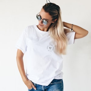Peut inclure: T-shirt blanc avec un petit motif circulaire portant l'inscription "Bride to Be" et un cœur. Le t-shirt est associé à un jean bleu. L'image montre une personne portant des lunettes de soleil et un serre-tête.