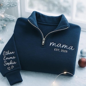 Puede incluir: Sudadera azul marino con cuello con cremallera. La palabra "mama" y "EST. 2026" están bordadas en blanco en la parte delantera. La manga izquierda tiene los nombres "Ethan, Emma, Sophia" bordados en blanco, con dos corazones.