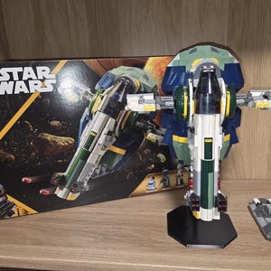 May include: A LEGO Star Wars Jango Fett's Starship building set, model 75433, featuring a 707-piece count. The set includes a constructed starship on a black display stand, a small grey vehicle with a minifigure, and the original product box.