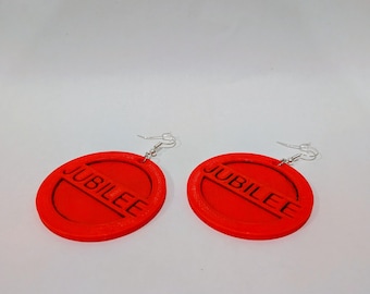 May include: A pair of red, circular earrings with the word "JUBILEE" embossed on each. The earrings have a silver-colored hook for pierced ears. The design is simple and bold.