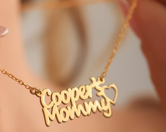 May include: A gold-colored necklace with the words "Cooper's Mommy" in a cursive font. A small heart shape is next to the word "Mommy". The necklace is on a delicate chain.
