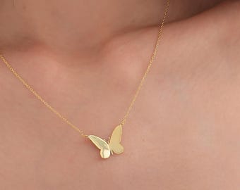 May include: A delicate gold-colored butterfly pendant necklace. The butterfly design is centered on a thin chain. The necklace is worn around the neck.