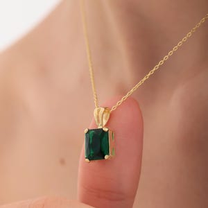 May include: A gold chain necklace with a square emerald green pendant.