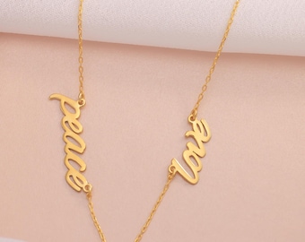 May include: A gold-colored necklace with the words "peace" and "love" in a cursive font. The necklace has a delicate chain and the words are connected by a small chain. The background is a soft pink color.