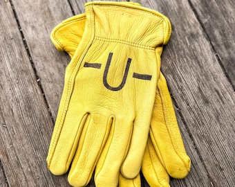 May include: A pair of yellow leather work gloves with the letter "U" printed on the back of the gloves.
