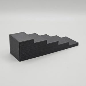 May include: A black, stepped display stand with six ascending levels. The stand is made of a solid, dark material and is designed to showcase small items. The steps gradually decrease in size, creating a tiered effect.