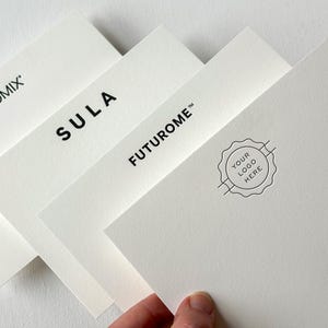 May include: A stack of white business cards with black text. The cards display the brand names "PROMIX", "SULA", and "FUTUROME". One card features a circular logo with the text "YOUR LOGO HERE".
