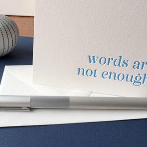 May include: A white card with the text "words are not enough." written in blue. A silver pen is lying on a white envelope.