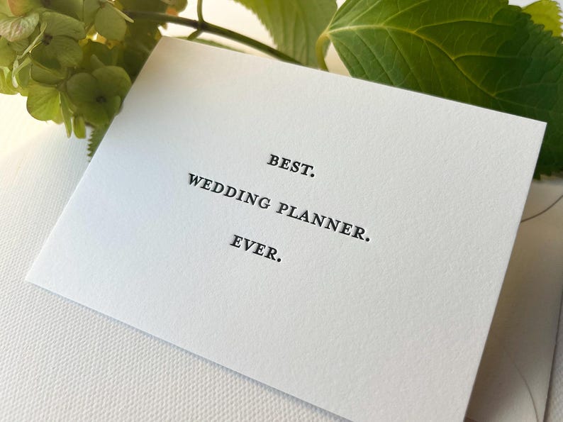 May include: A white card with black text that reads "BEST. WEDDING PLANNER. EVER."