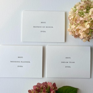 May include: Three white cards with black text. The top card says "BEST. MATRON OF HONOR. EVER.". The middle card says "BEST. WEDDING PLANNER. EVER.". The bottom card says "BEST. DREAM TEAM. EVER."