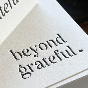May include: A white ceramic mug with a black handle and the text "But First, Coffee" in a black, handwritten-style font. The mug is on a white surface.