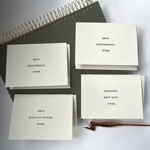 May include: Four white cards with black text on a green background. The cards read "Best. Bridesmaid. Ever.", "Best. Maid of Honor. Ever.", "Best. Groomman. Ever.", and "Greatest. Best Man. Ever."