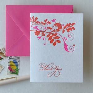 May include: A white thank you card with a pink and orange floral design. The card has the words "Thank You" printed in pink.