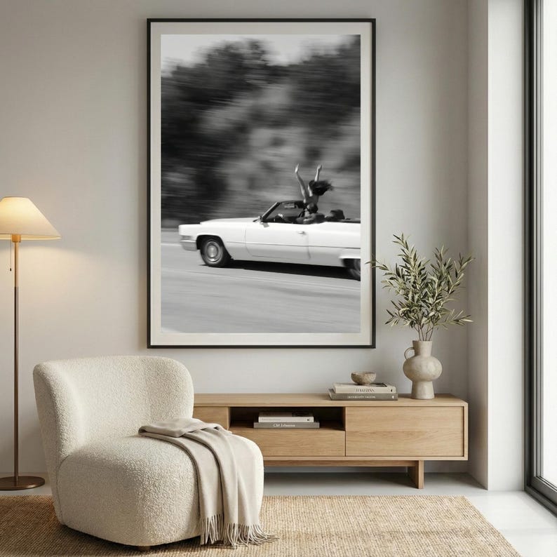 May include: Monochrome framed print featuring a white convertible car speeding along a road. A person stands in the car with arms raised. The background shows blurred trees.