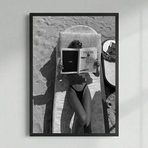 Peut inclure: Impression encadr&eacute;e en noir et blanc d'une personne lisant un magazine intitul&eacute; "THE VIBE" en prenant un bain de soleil. La personne porte des lunettes de soleil et un maillot de bain noir. Vue de haut.