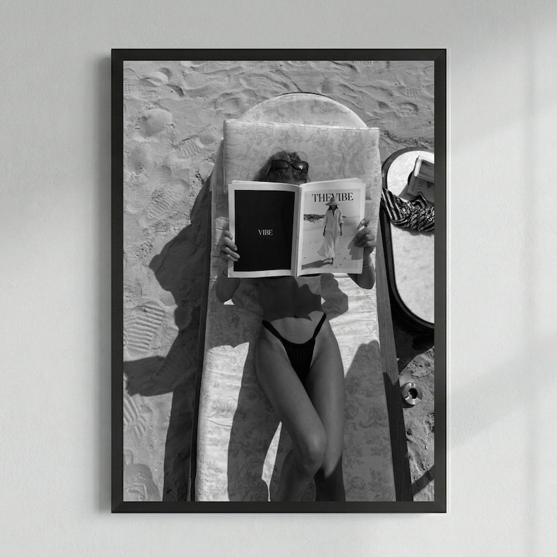 Peut inclure: Impression encadr&eacute;e en noir et blanc d'une personne lisant un magazine intitul&eacute; "THE VIBE" en prenant un bain de soleil. La personne porte des lunettes de soleil et un maillot de bain noir. Vue de haut.