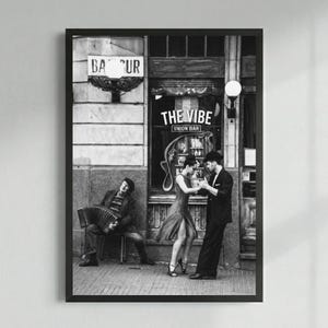 May include: Black and white framed print depicting a street scene with a bar called "The Vibe Union Bar." A couple dances tango in front of the bar, while a musician plays an accordion. The image has a vintage, classic feel.