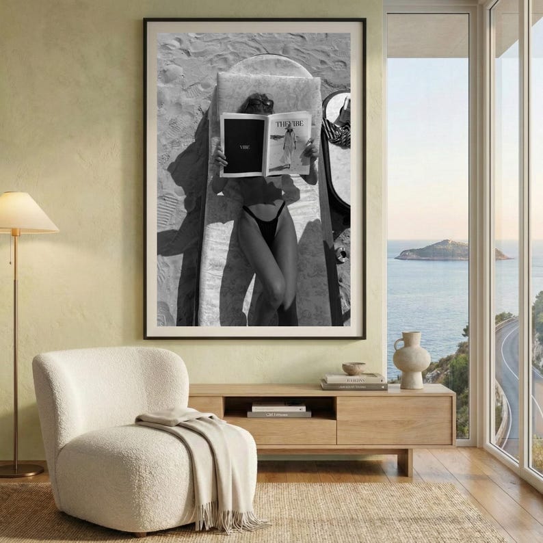 Peut inclure: Impression en noir et blanc encadr&eacute;e d'une personne lisant un magazine sur une plage. Le magazine affiche le texte "THE VIBE". La personne porte un maillot de bain noir et est allong&eacute;e sur une chaise longue.