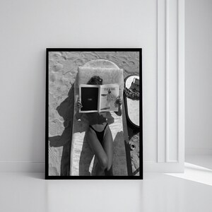 Peut inclure: Impression encadr&eacute;e en noir et blanc d'une personne allong&eacute;e sur une chaise longue, lisant un magazine. Le magazine ouvert affiche le mot "Vibe". Un miroir et un chapeau sont &eacute;galement visibles.