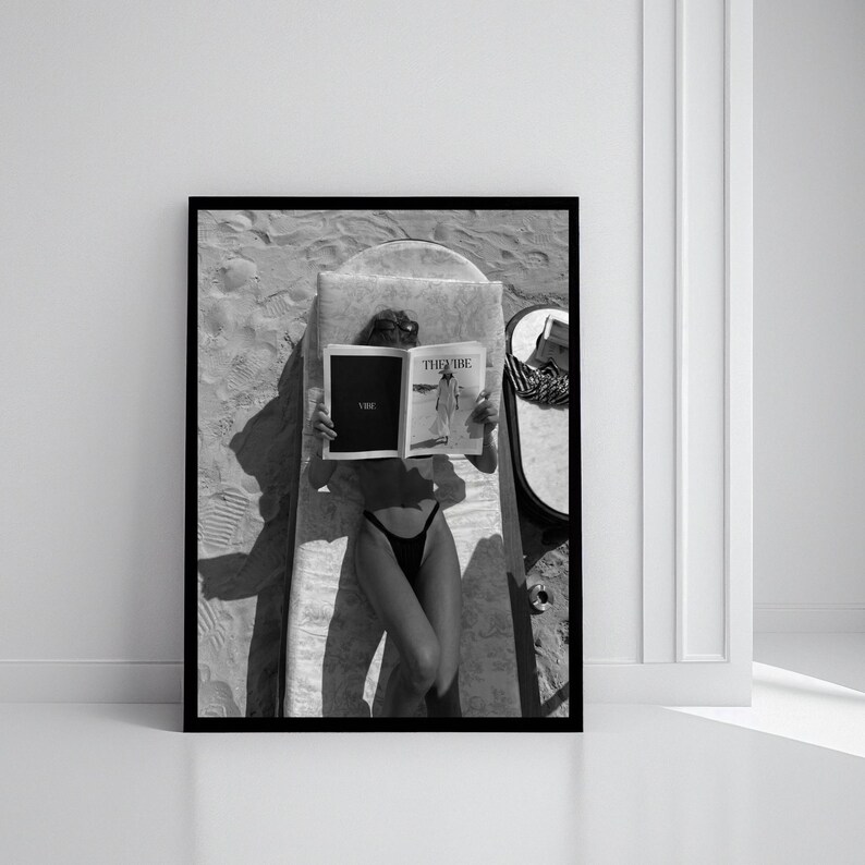 Peut inclure: Impression encadr&eacute;e en noir et blanc d'une personne allong&eacute;e sur une chaise longue, lisant un magazine. Le magazine ouvert affiche le mot "Vibe". Un miroir et un chapeau sont &eacute;galement visibles.