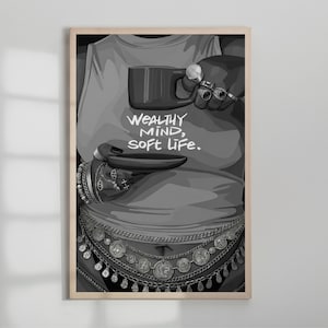 May include: Black and white art print featuring a person wearing a tank top with the text "WEALTHY MIND, SOFT LIFE." The person is adorned with jewelry and holding a mug and a small plate. The artwork is framed in a light wood.