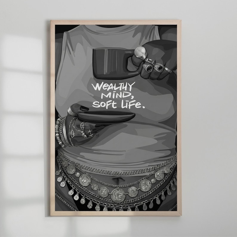 May include: Black and white art print featuring a person wearing a tank top with the text "WEALTHY MIND, SOFT LIFE." The person is adorned with jewelry and holding a mug and a small plate. The artwork is framed in a light wood.
