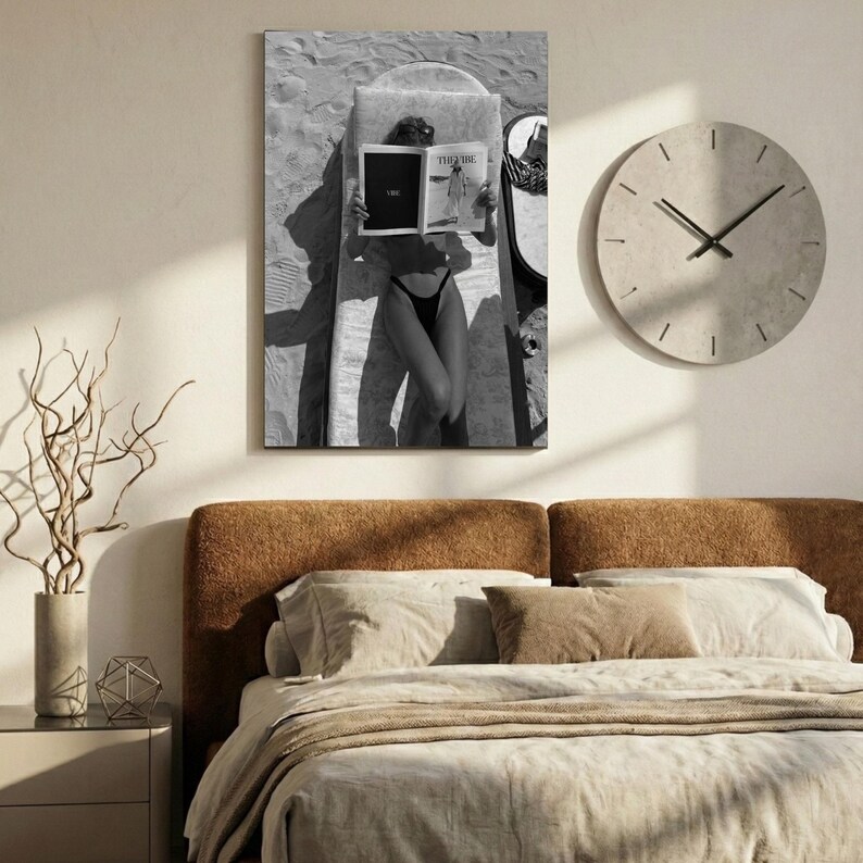 Peut inclure: Photographie en noir et blanc d'une personne lisant un magazine sur une chaise longue. L'image est un gros plan, avec la personne et le magazine occupant la majeure partie du cadre. Une grande horloge ronde est sur le mur. Un lit est au premier plan.