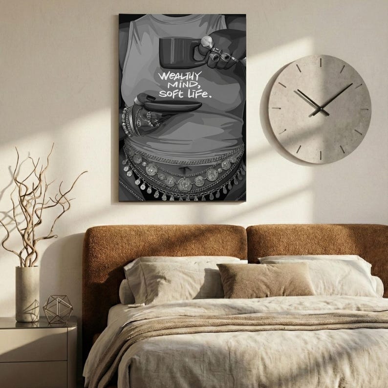May include: Black and white wall art print featuring a person holding a mug, with the text "WEALTHY MIND, SOFT LIFE." The artwork includes jewelry and a decorative belt. A round clock is visible on the wall.