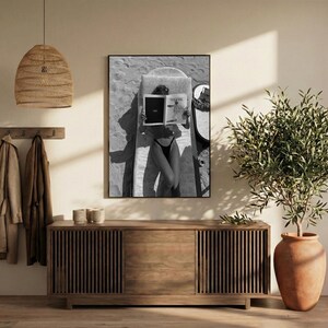 Peut inclure: Impression en noir et blanc encadr&eacute;e d'une personne lisant un magazine sur une planche de surf. L'image est prise d'en haut, montrant la personne en maillot de bain noir. La couverture du magazine est visible, avec le mot "THE" affich&eacute;.