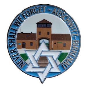 Könnte beinhalten: Eine blaue und silberne Emaille-Anstecknadel mit einem weißen Davidstern und einer Darstellung des Tores des Konzentrationslagers Auschwitz-Birkenau. Der Text um die Anstecknadel lautet "Never Shall We Forget - Auschwitz-Birkenau".
