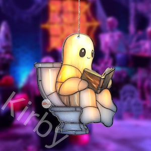 May include: A quirky stained-glass decoration depicting a smiling, yellow ghost reading a book whilst seated on a toilet. The ornament hangs from a silver chain. The design includes the text "2Dilat" and "Kirby".
