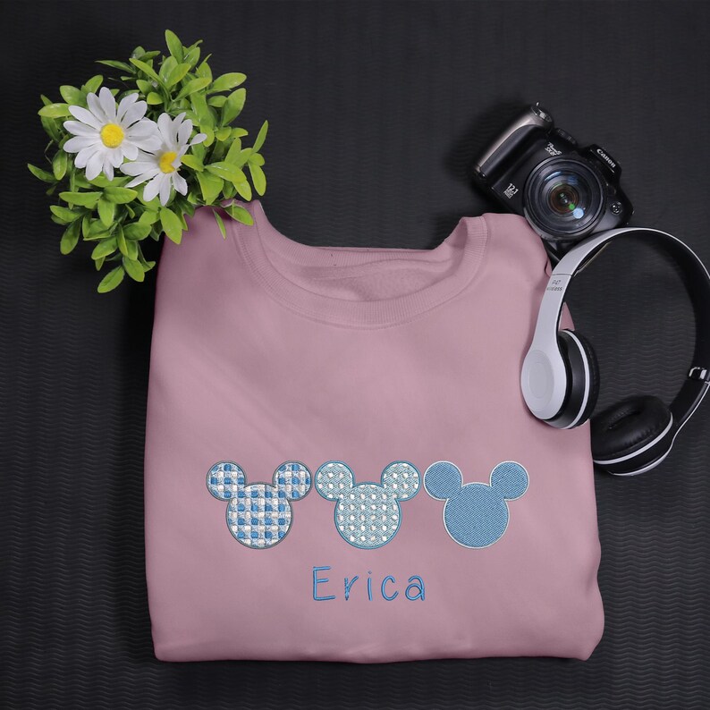 May include: A pink sweatshirt with three blue embroidered Mickey Mouse heads and the name "Erica" embroidered below.