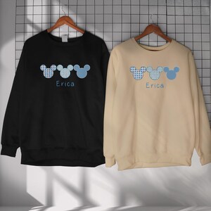 May include: Two black and beige sweatshirts with a blue and white Mickey Mouse design and the name "Erica" printed on each.