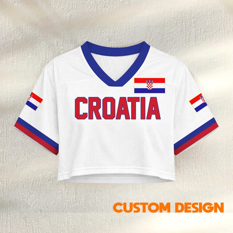 K&ouml;nnte beinhalten: Wei&szlig;es Crop-Jersey mit dem Wort "CROATIA" in roten Blockbuchstaben. Das Trikot hat einen blauen V-Ausschnitt und rot-blaue Verzierungen an den &Auml;rmeln. Die kroatische Flagge ist auf der Brust und den &Auml;rmeln abgebildet. Der Text "CUSTOM DESIGN" steht unten.
